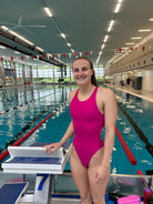 Frau im pinken Badeanzug steht am Startblock in der Schwimmhalle